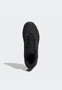 Zapatilla deportiva negra con una superficie texturizada, punta redondeada, cierre de cordones tradicional y un collar acolchado para mayor comodidad.