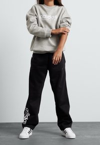 Šedá mikina s bílým logem "adidas", spojená s černými tepláky s detailním logem, a bílé tenisky s černými pruhy.