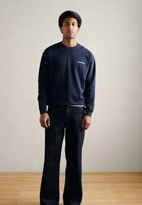 Tmavomodrá mikina s okrúhlym výstrihom a jemným logom na hrudi v kombinácii s voľne strihanými čiernymi džínsami z denimu, oboje z mäkkých látok.