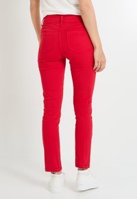 Los jeans skinny de denim rojo presentan un cintura alta, dos bolsillos traseros, una textura suave y se combinan con zapatillas blancas.