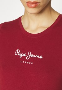 Burgundi spalvos medvilninis marškinėlis su apvaliu iškirpimu ir baltu logotipu, kuriame parašyta "Pepe Jeans LONDON", centroje ant krūtinės.