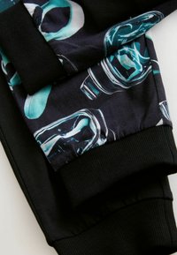 Svarta träningsbyxor har ett färgglatt mönster med abstrakta former i teal och vitt. Klämmorna är ribbade, vilket ger en tight passform.