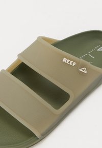 Sandală verde tip slide, cu trei curele late, fabricată din plastic texturat. Prezintă un mic logo alb "REEF" și o talpă interioară netedă.
