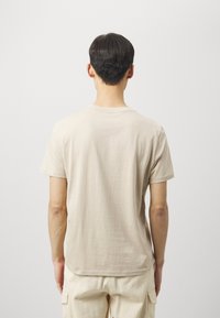 Beige cotton t-shirt with short sleeves, crew neckline, and a relaxed fit. Smooth texture with a simple, unembellished design.