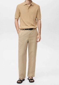 Polo à manches courtes beige à côtes, pantalon beige ample, ceinture noire et sandales noires. Texture lisse, design minimaliste, sans motifs visibles.