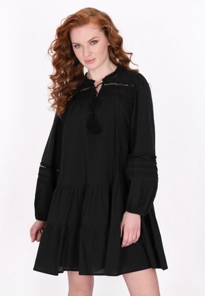 Rochie neagră cu un design în straturi, mâneci lungi, accente din dantelă și închidere cu panglică la gât. Material moale cu o croială lejeră.