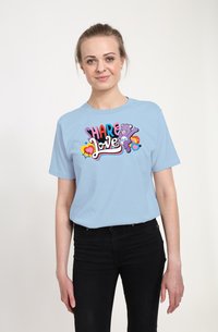 Lyseblå t-shirt med korte ærmer med et farverigt "Del kærlighed" grafik, som inkluderer en bjørn og hjerter, parret med sorte jeans.