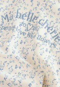 Tissu blanc avec un motif floral bleu. Le texte dit "Ma belle chérie répands l'amour comme des fleurs", avec des accents de broderie décorative.