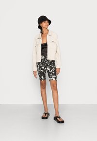 Casaco texturizado em creme, camisola de cetim preta, calções de bicicleta em mármore preto e branco, e sandálias de plataforma pretas; usado com um chapéu de balde preto.