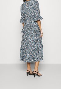 Blommönstrad midikjol i blått med volangärmar och nyckelhål i ryggen. Tillverkad av lättviktig tyg med ett lager-på-lager nederdel. Svarta högklackade skor.