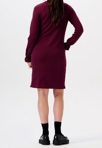 Burgundské šaty s dlouhými rukávy, na manžetách staženými, slim fit, délka do poloviny stehen a hladký materiál. V kombinaci s černými botami a ponožkami.