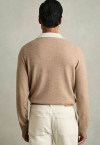 Pull en laine beige avec un col blanc, des manches ajustées et une texture douce. Assorti à un pantalon de couleur claire avec des poches arrière.