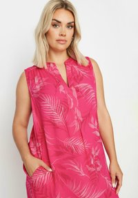 Fuchsiasärmmös klänning med V-hals, har ett bladmönster, sidofickor och en avslappnad passform. Tillverkad av lätt, texturerad tyg.