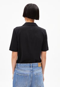 Black short-sleeve polo shirt with a collar, paired with light blue high-waisted denim shorts featuring a leather patch and double back pockets.