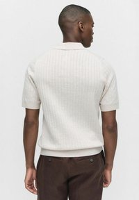 Kortärmad polotröja i beige med ribbad textur. Har en klassisk krage och figursydd midja. Matchas med bruna byxor.