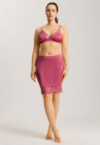 Bralette de satén rosa con detalles de encaje y tirantes ajustables, combinado con una falda corta de satén rosa a juego que presenta un borde de encaje en el dobladillo.