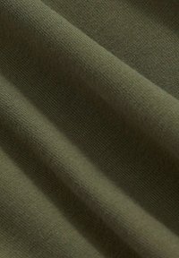 Olivi vihreä kangas, jossa on pehmeä, teksturoitu kudonta. Materiaali on kevyt ja laskeutuu saumattomasti hienovaraisilla sävyeroilla.