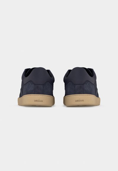 Paire de baskets basses en daim bleu foncé avec semelles beige, vue de dos, présentant "HOGAN" en relief sur le talon.