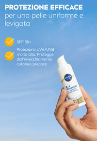 Bottiglia cilindrica bianca di NIVEA con primer solare, con dettagli blu e oro, etichettata "2 in 1 Primer UV Serum", tenuta contro un cielo blu.