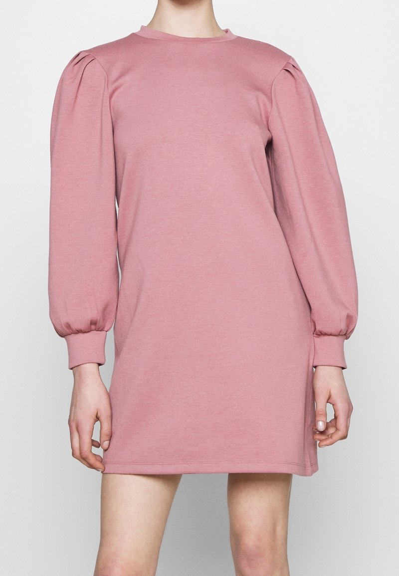Robe à manches bouffantes roses en tissu doux. Elle possède un col rond et une coupe décontractée, avec des détails froncés aux épaules.