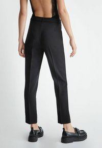 Pantaloni neri su misura con una vestibilità slim, caratterizzati da una texture liscia, una leggera lucentezza e un design pulito e minimalista. Indossati con scarpe plateaux nere.