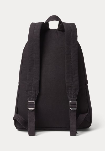 Mochila de tela negra con correas acolchadas para los hombros, ajustadores metálicos y una asa superior para llevar, mostrada desde atrás sobre un fondo blanco.