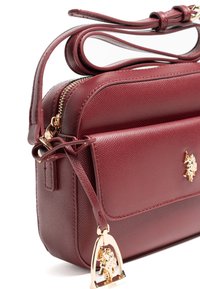Burgundowa skórzana torba na ramię z teksturowanym wykończeniem, złotym metalowym okuciem, zamkiem błyskawicznym oraz zewnętrzną kieszenią z zawieszką z logo.