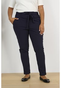 Marineblå skræddersyede bukser med bindebånd i taljen, der har sidelommer og en slim fit-design, suppleret med sorte flade sko.