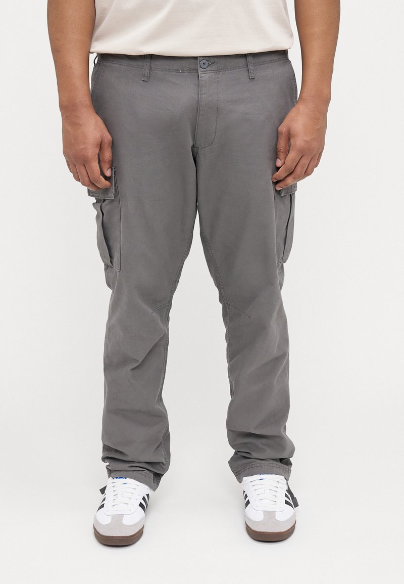 Grijze cargo-broek met een ontspannen pasvorm, voorzien van meerdere zijzakken, gestikte details en een versleten stofstructuur. Gecombineerd met witte sneakers.