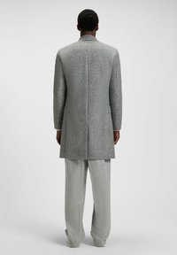 Grå vävd kappa med lång silhuett, som har en subtil textur och skräddarsydd bakseam, i kombination med matchande ljusgrå byxor.