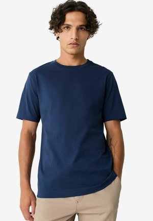 Camiseta de algodón de color azul marino con cuello redondo, mangas cortas y una textura suave. Corte ligeramente relajado con un dobladillo que curvaba hacia abajo.