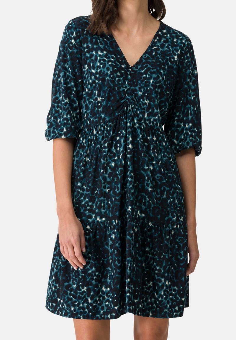 Femme portant une robe courte imprimée léopard vert sarcelle foncé et noir avec des manches trois-quarts et un col en V.
