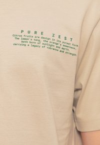 Μπεζ ύφασμα με πράσινο κείμενο που γράφει «PURE ZEST» και μια περιγραφή του σχεδίου, της γεύσης και της φυσικής προέλευσης των εσπεριδοειδών.