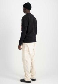 Felpa nera con collo rotondo e tasca con zip sulla manica sinistra, abbinata a pantaloni cargo larghi di colore crema e scarpe nere.