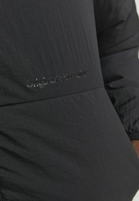 Black jacket featuring a textured fabric with a matte finish. Embroidered logo "Original Studio™" in a subtle, slightly raised design.