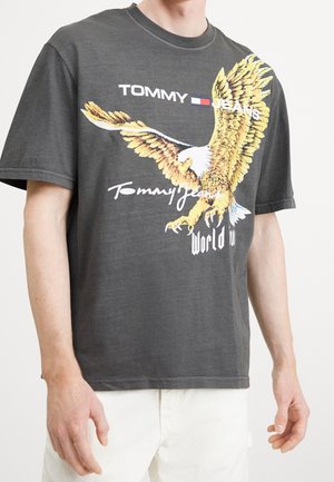 Ciemnoszary t-shirt z grafiką żółtego orła, logo „Tommy Jeans” oraz napisem „World”. Krótkie rękawy i okrągły dekolt.