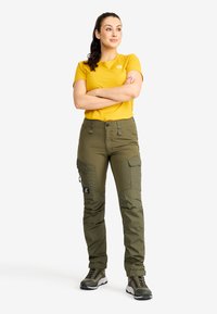 Olivgrön cargobyxor med flera fickor, i kombination med en gul t-shirt. Outfiten har en avslappnad passform och slitstukt materiaal.