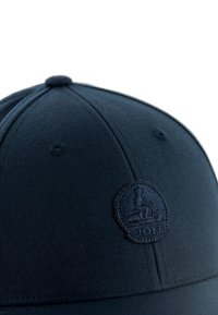 Marineblauwe baseballpet van stof, met een rond geborduurd logo aan de voorkant en een gladde textuur met gestikte accenten.