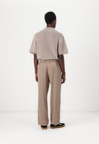 Short-sleeve, beige patterned knit shirt paired with light brown, loose-fitting pants and black sneakers with a white logo and brown soles.