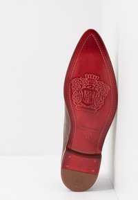 Semelle de chaussure en cuir marron de forme pointue, présentant un accent en cuir rouge, un logo embossé et la taille « 41 » clairement visible.