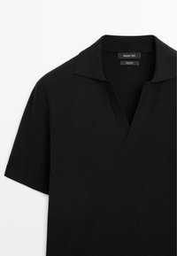 Polo shirt in cotone nero con tessuto testurizzato, maniche corte e scollatura a V. Include un colletto piatto e un'etichetta del marchio discreta.