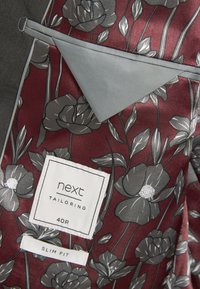 Tissu bordeaux à motifs floraux dans des nuances de gris ; comprend un mouchoir de poche gris et une étiquette en tissu indiquant la taille et la coupe.