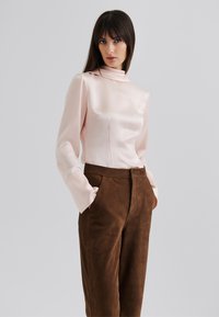 Pink satin blouse with ribbed texture and high collar, paired with brown suede trousers, featuring side pockets and tailored fit.