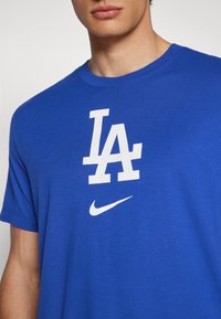 Kék pamut póló, nagy fehér "LA" grafikával és egy kis fehér Nike swoosh logóval az elején. Rövid ujjú és kerek nyakú kialakítás.
