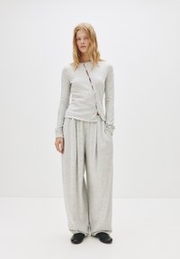 Helles graues gestricktes Langarmoberteil mit vorderen Knöpfen und passenden lockeren Hosen. Glatte Textur mit leichtem Fall und seitlichen Taschen. Schwarze Schuhe.