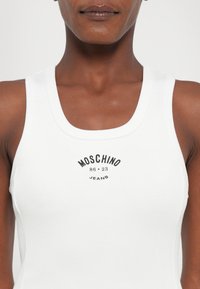 Balta išilgine tekstūra marškinėlių su apvalia iškirpte ir juodu spaudiniu virš krūtinės, kuriame parašyta "MOSCHINO 86-23 JEANS."