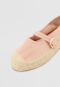 Világos rózsaszín vászon espadrille, kerek orral, jutából készült talppal és csatos pánttal a lábfej fölött.