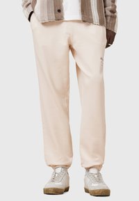 Lichtroze sweatpants gemaakt van zachte stof, met een elastische tailleband en boorden. Gecombineerd met grijze en witte sneakers.