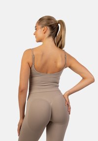 Beige, aansluitend tanktop met dunne bandjes, gecombineerd met bijpassende hoge taille leggins. Gladde textuur, naadloos ontwerp en contourerende details.