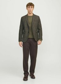 Blazer en tweed marron avec revers à cran, associé à un pull en tricot vert olive et un pantalon marron foncé, porté avec des chaussures sombres.